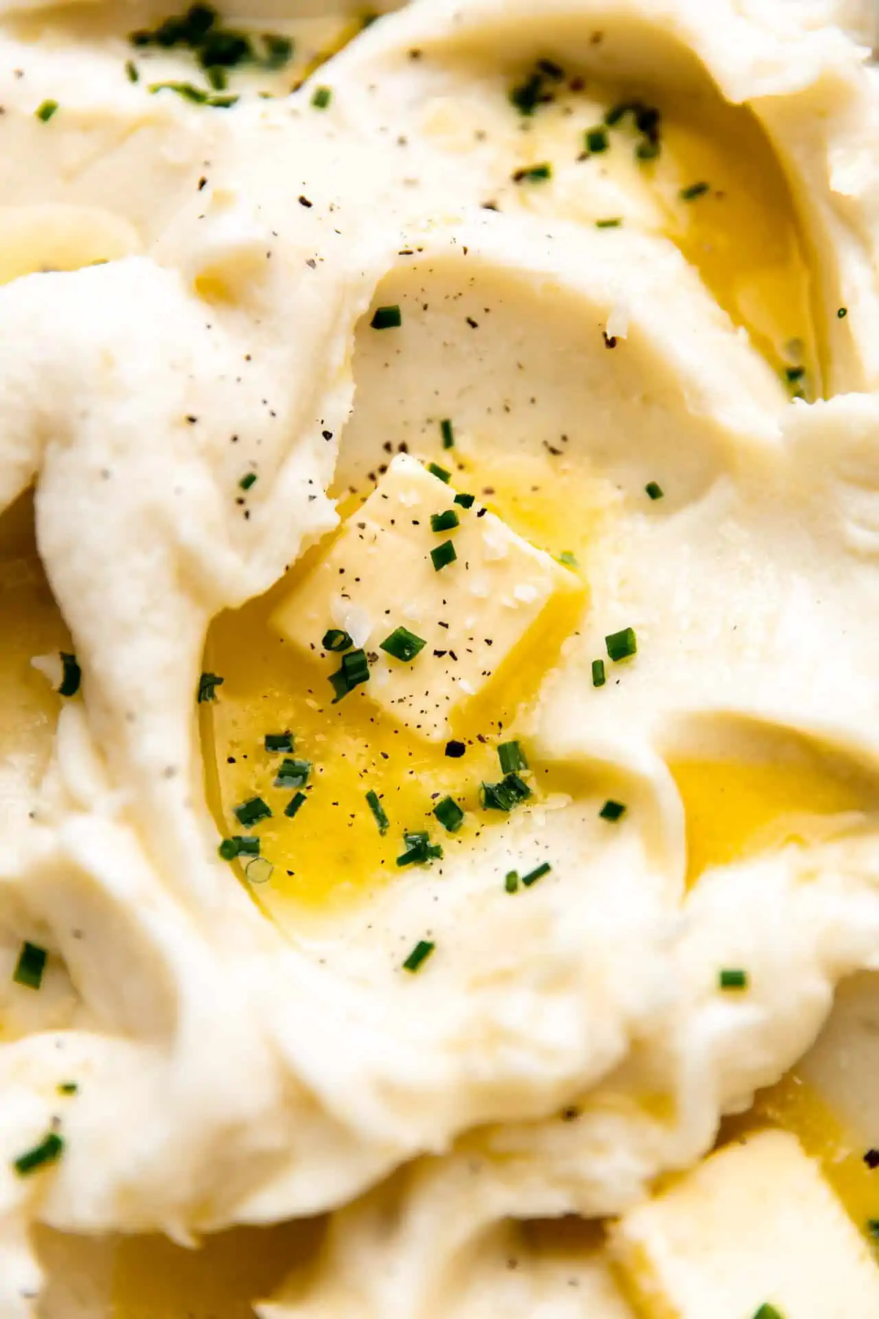 Up close of creamy mashed potatoes topped with butter, fresh chives and cracked pepper.