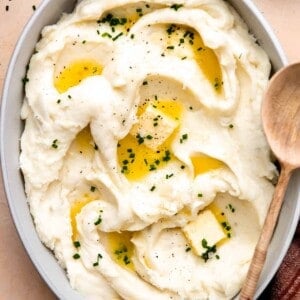 Dish filled with creamy mashed potatoes swirled and topped with melted butter and fresh chives.