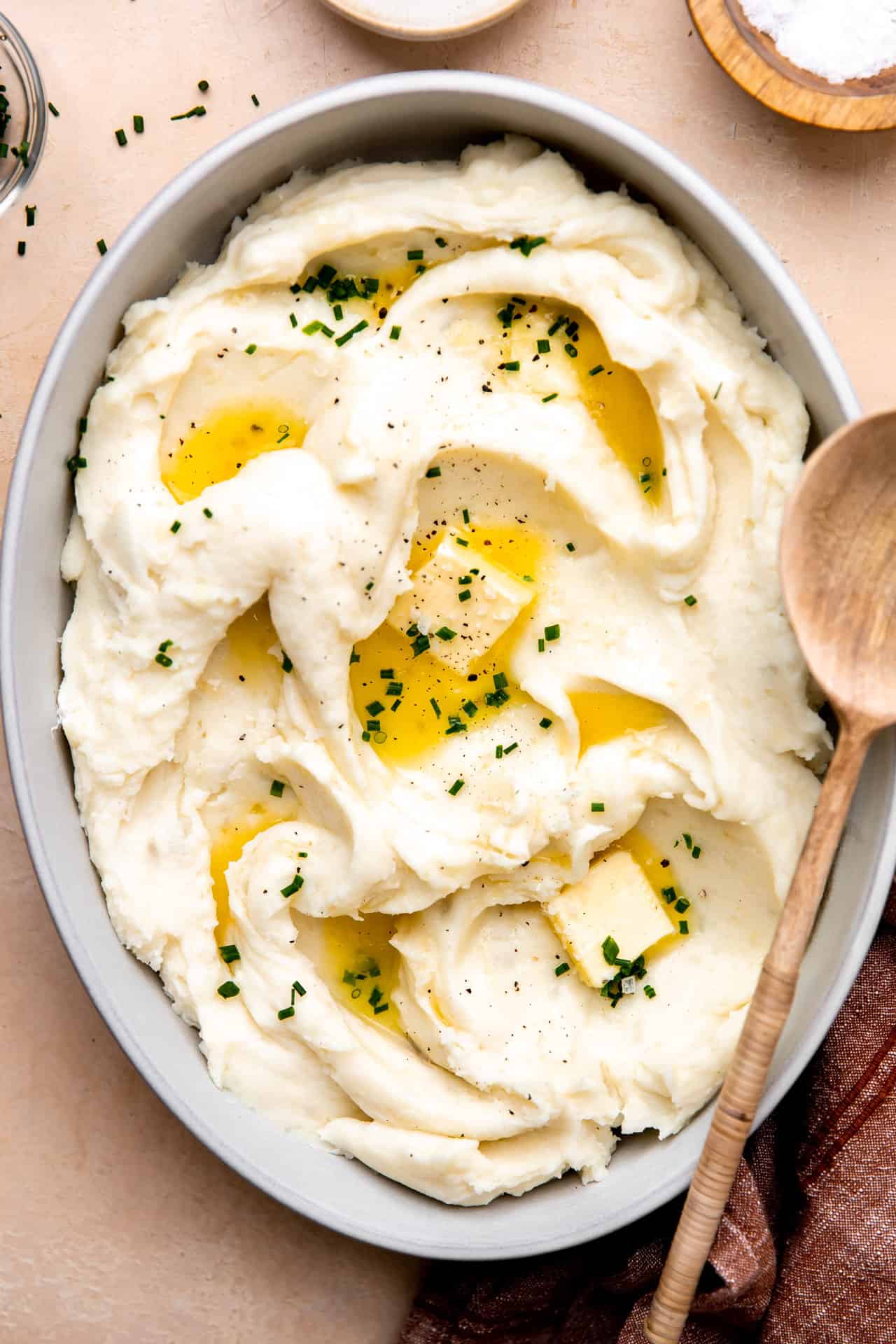 Dish filled with creamy mashed potatoes swirled and topped with melted butter and fresh chives.