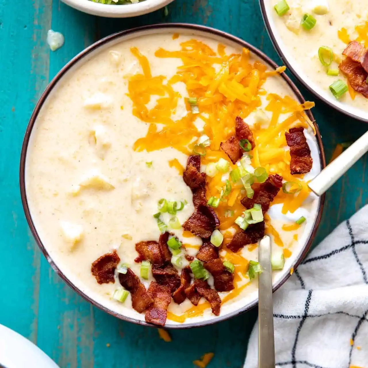 Bowl of potato soup topped with melted cheddar cheese, sour cream, diced bacon and green onion.