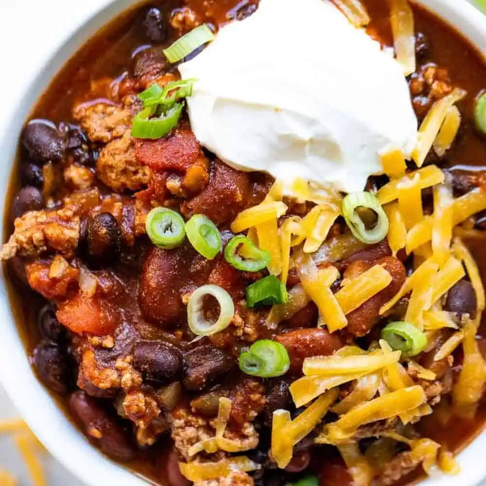 Bowl filled with turkey chili, topped with sour cream, onion and cheese.