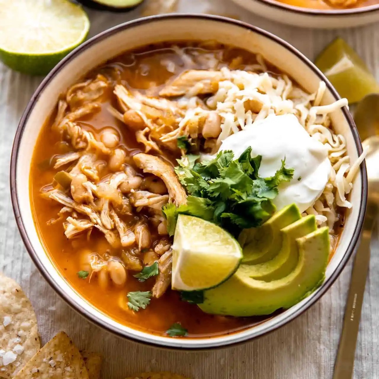 Bowl filled with white chicken chili and topped with cheese, sour cream and avocado.
