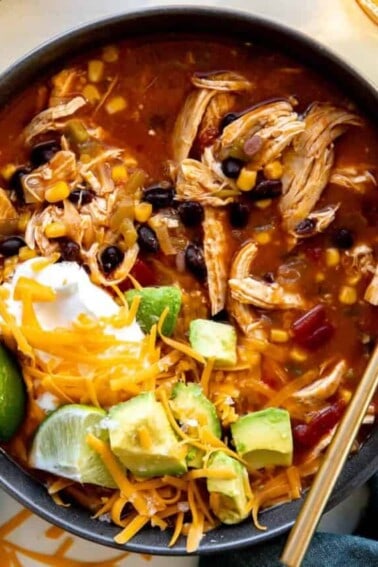 Bowl of chicken enchilada soup topped with cheese, sour cream and avocado.