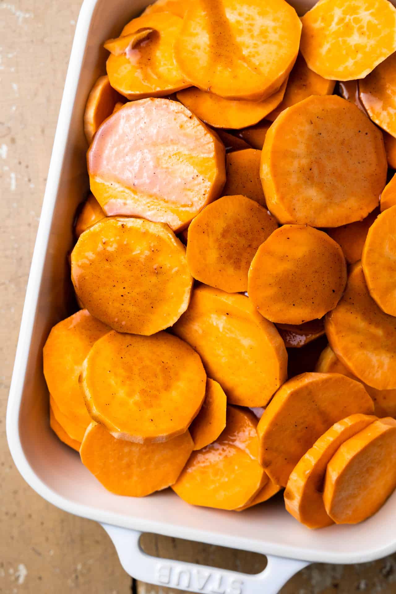 Brown sugar sauce poured over sliced sweet potato in a baking dish.