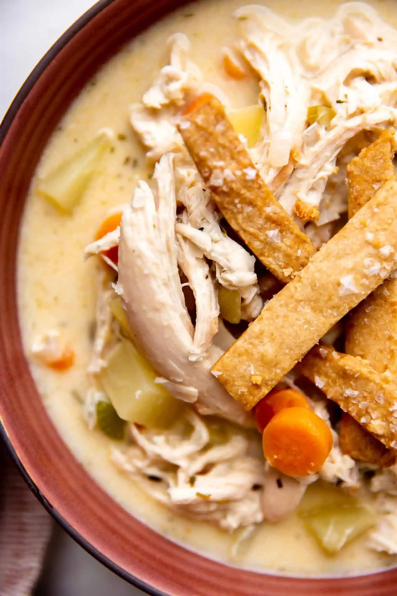 Up close view of chicken pot pie soup in a bowl topped with pie crust crackers. 