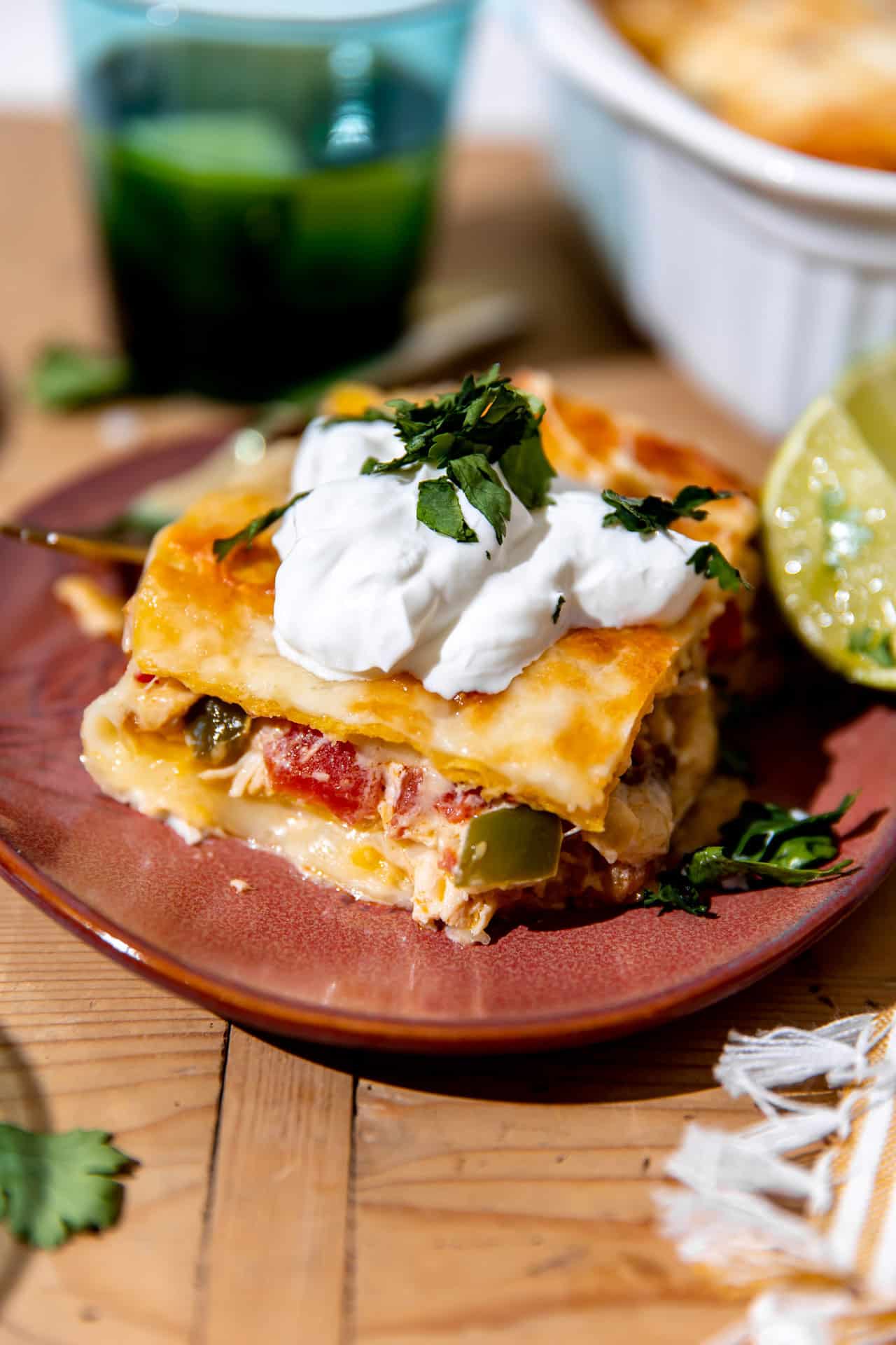 Slice of King ranch casserole served on a plate and topped with sour cream and fresh cilantro.