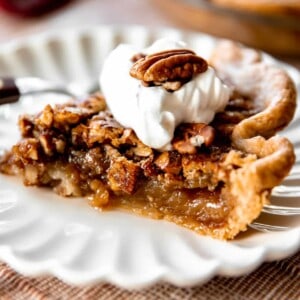 Slice of pecan pie topped with a swirl of whipped cream and a halved pecan on top.
