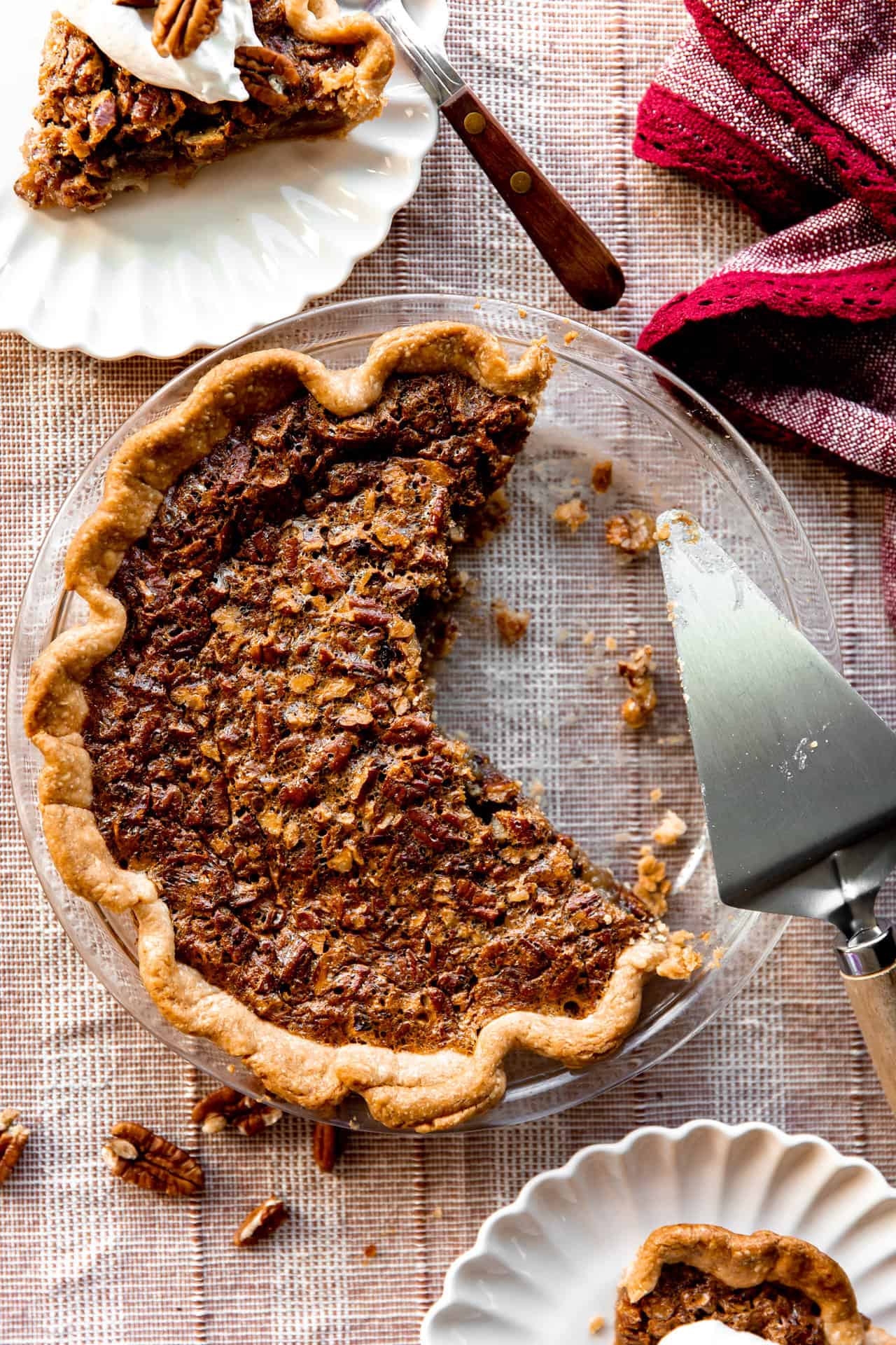 Baked pecan pie in a glass dish with slices removed and a pie server.