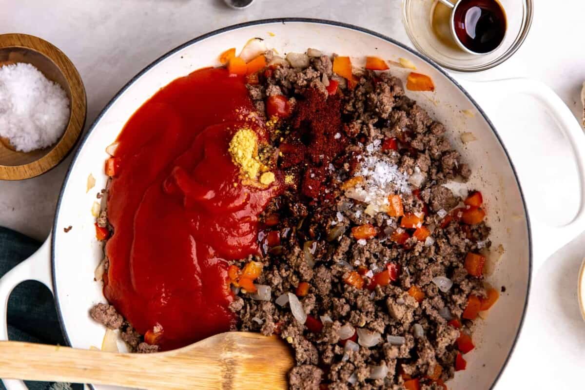 Ground beef in a skillet with homemade sloppy Joe sauce being added.