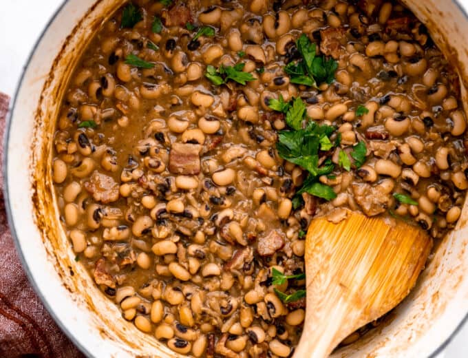 Pot filled with cooked black eyed peas with chunks of ham and bacon, topped with cilantro.