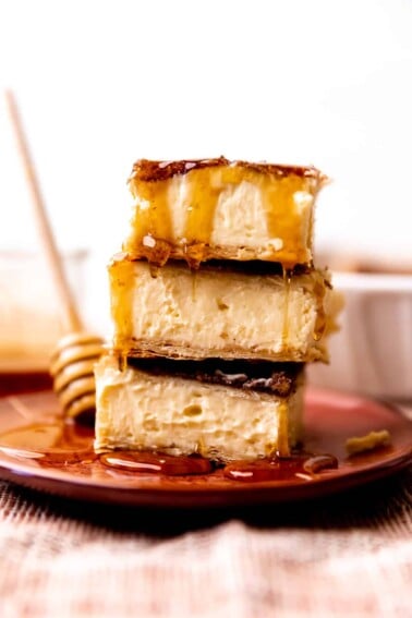 Stack of sopapilla cheesecake bars being drizzled with honey.