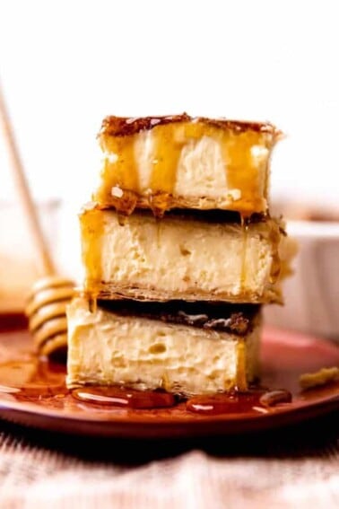 Stack of sopapilla cheesecake bars being drizzled with honey.