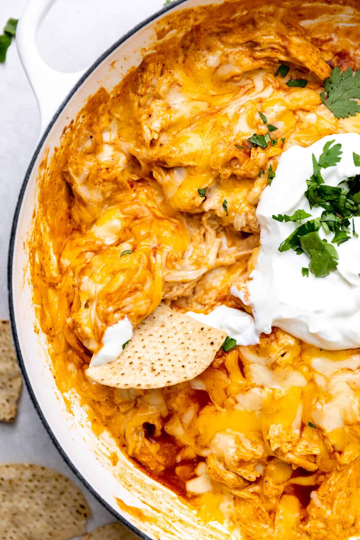 Up close of tortilla chip dipping into enchilada dip topped with sour cream and cilantro.