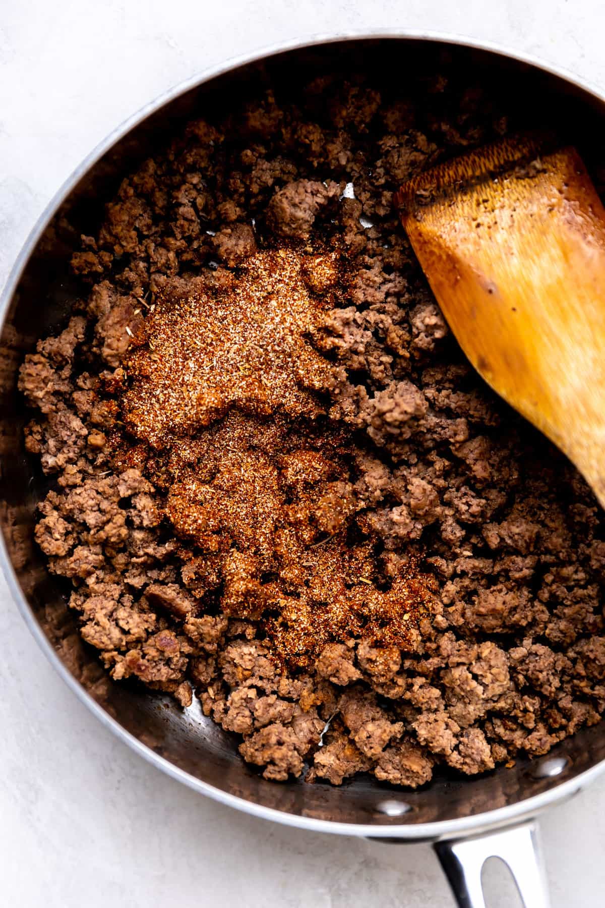 Ground beef cooked in a skillet with taco seasoning being added. 