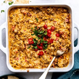 White baking dish filled with baked rotel dip topped with cilantro and chopped tomatoes.