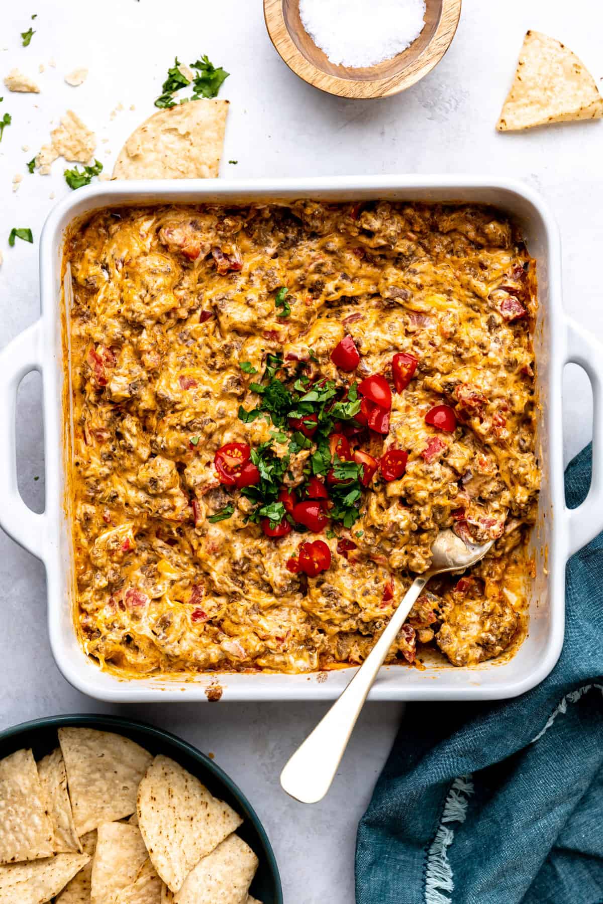 White baking dish filled with baked rotel dip topped with cilantro and chopped tomatoes. 