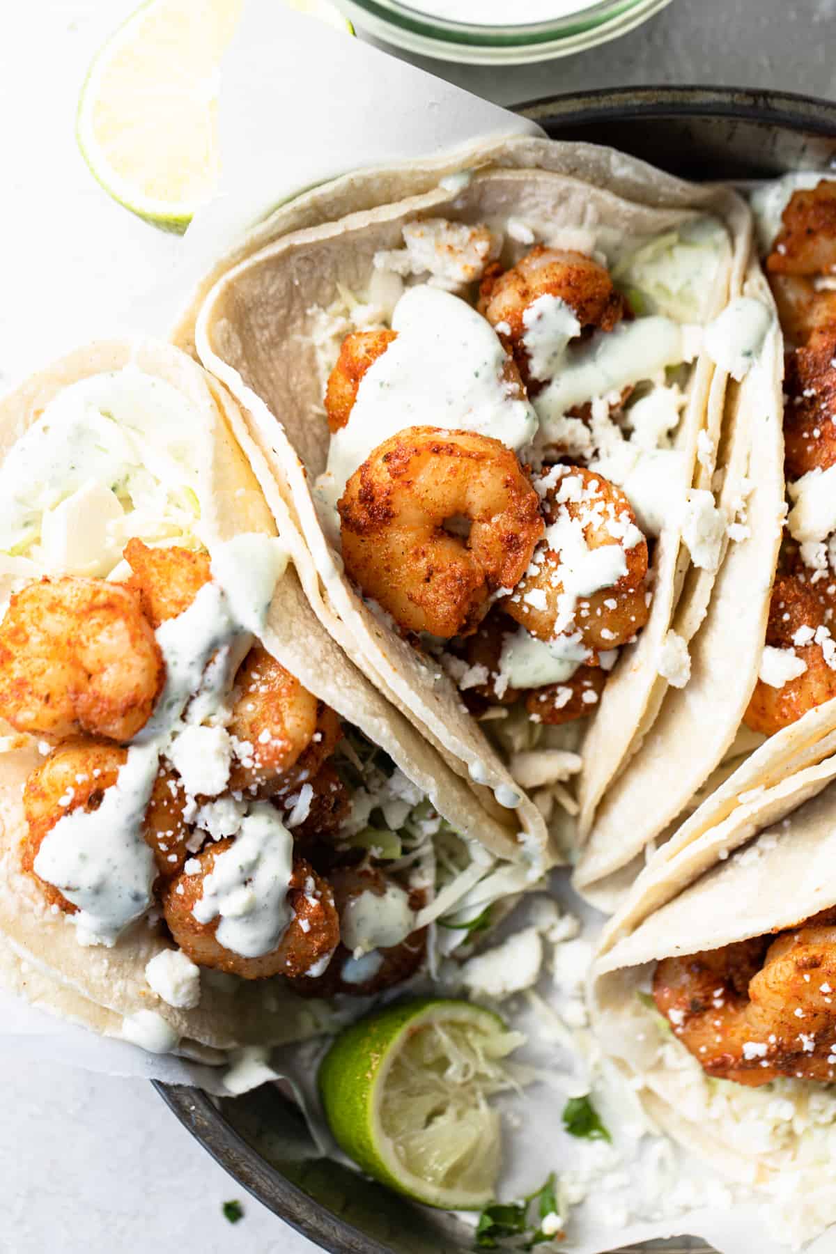 Tray filled with tacos de camarones with cabbage, queso fresco and a cilantro lime sauce drizzle.