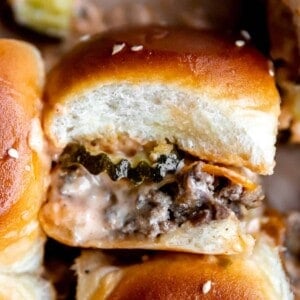 Up close cheeseburger slider on hawaiian rolls showing layers of ground beef, cheese, pickles and burger sauce.