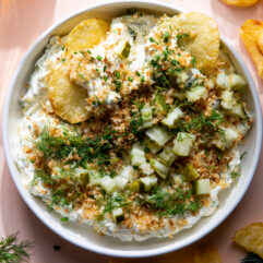 Bowl of dill pickle dip topped with toasted pinko, fresh dill and chives.