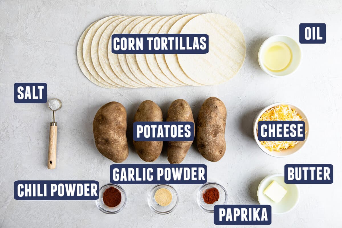 Ingredients needed to make fried potato tacos laid on the counter. Corn tortillas, potatoes, oil, cheese, butter, paprika, garlic powder, chili powder, salt.