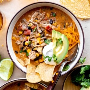 Bowl of chicken taco soup topped with tortilla chips, sour cream and sliced avocado.