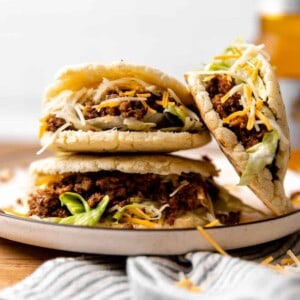 Stack of gorditas with ground beef filling with shredded lettuce and cheese.