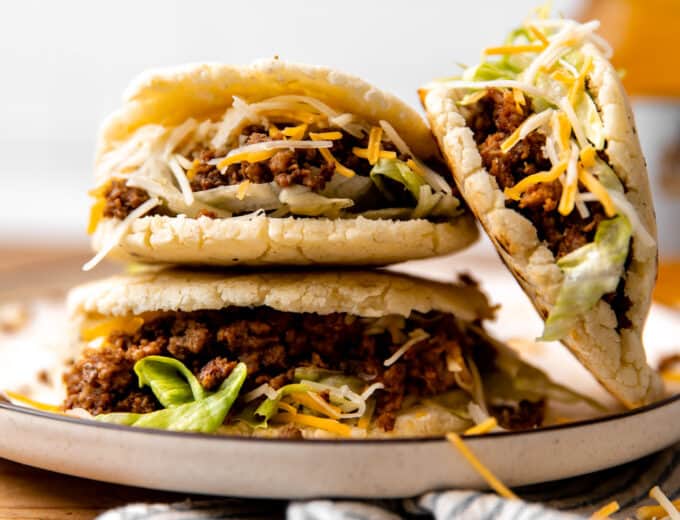 Stack of gorditas with ground beef filling with shredded lettuce and cheese.