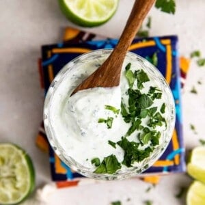 Glass filled with cilantro lime crema topped with fresh diced cilantro and a wooden spoon to serve.