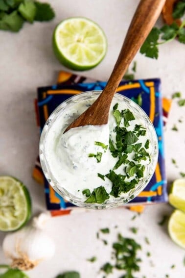 Glass filled with cilantro lime crema topped with fresh diced cilantro and a wooden spoon to serve.