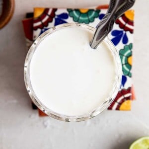 Overhead of a glass filled with mexican cream sauce with a spoon dipping in.