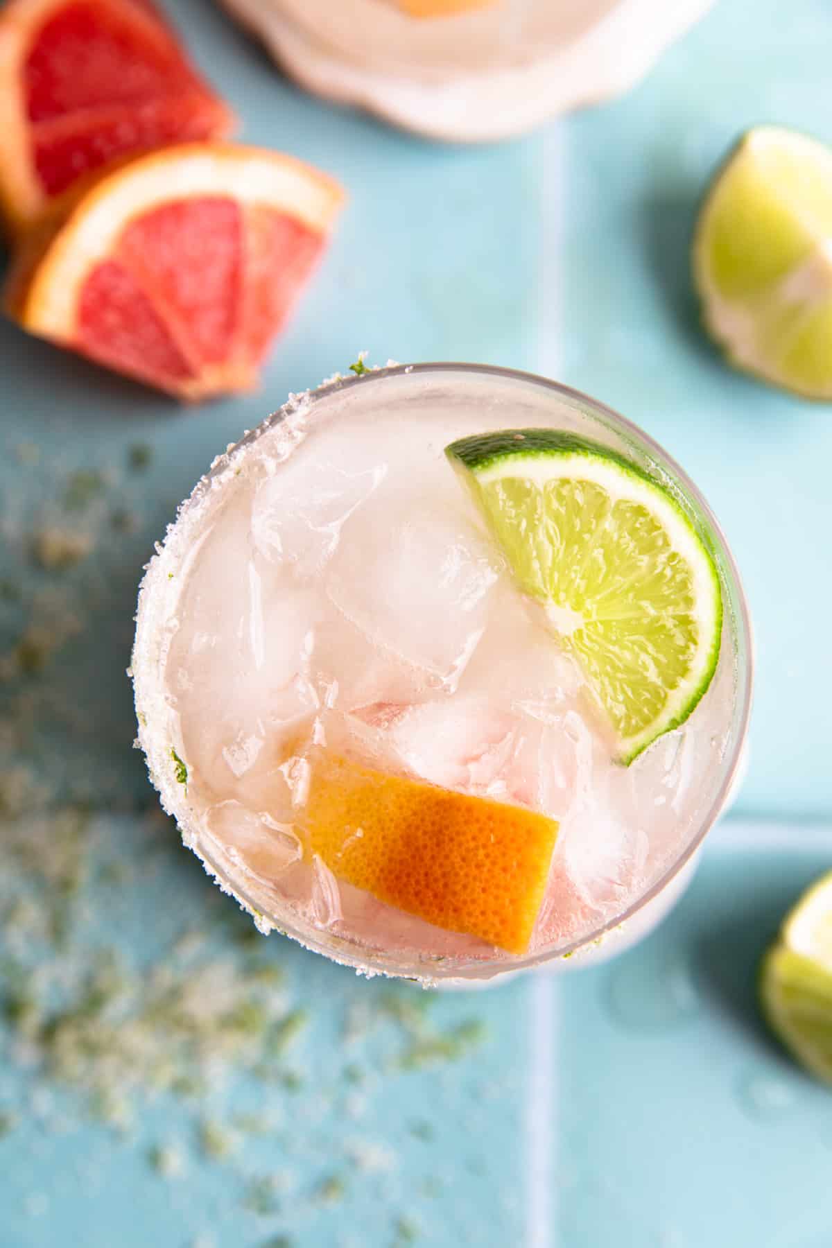 Overhead of a grapefruit paloma topped with fresh lime and grapefruit wedges.