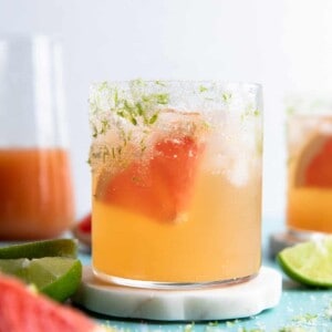 Glass on a coaster filled with grapefruit paloma on ice and a wedge of fresh grapefruit.