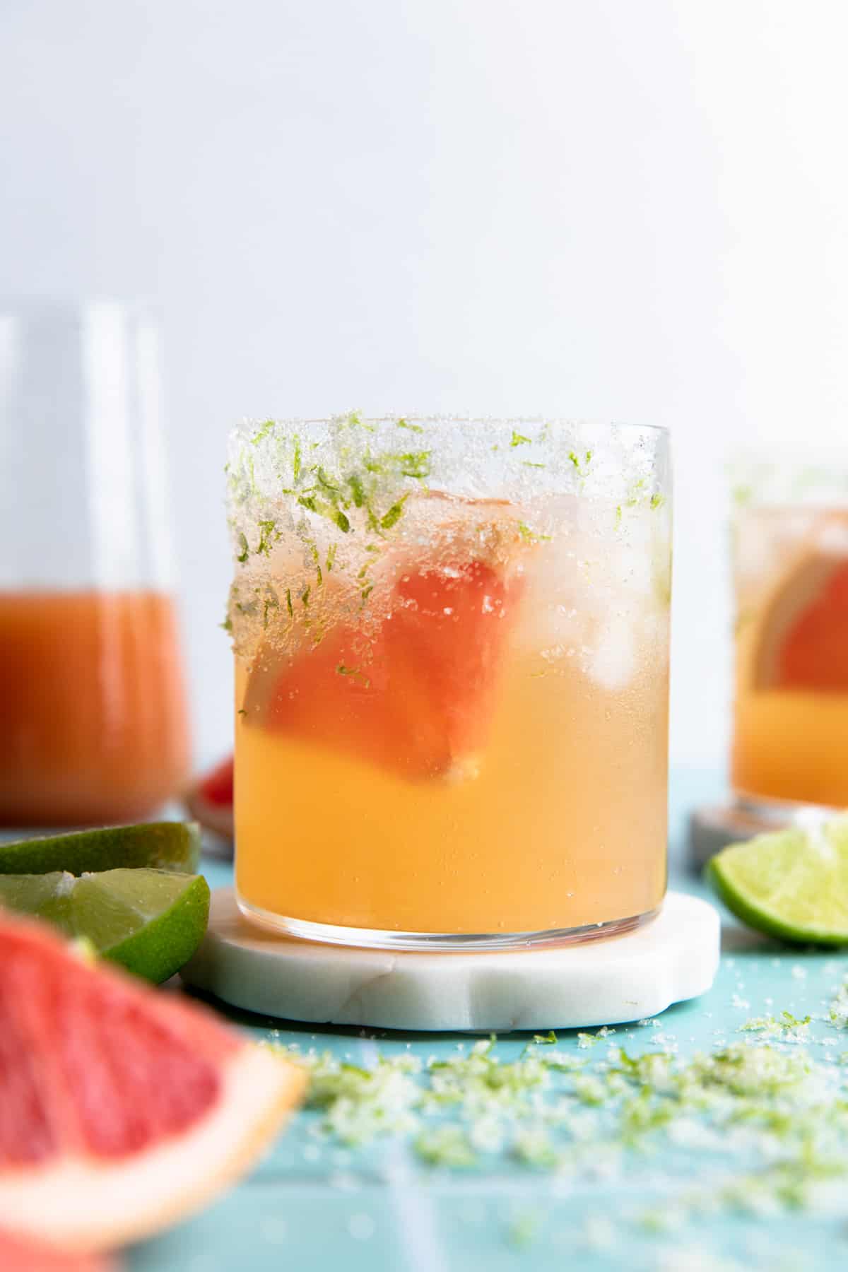 Glass on a coaster filled with grapefruit paloma on ice and a wedge of fresh grapefruit.