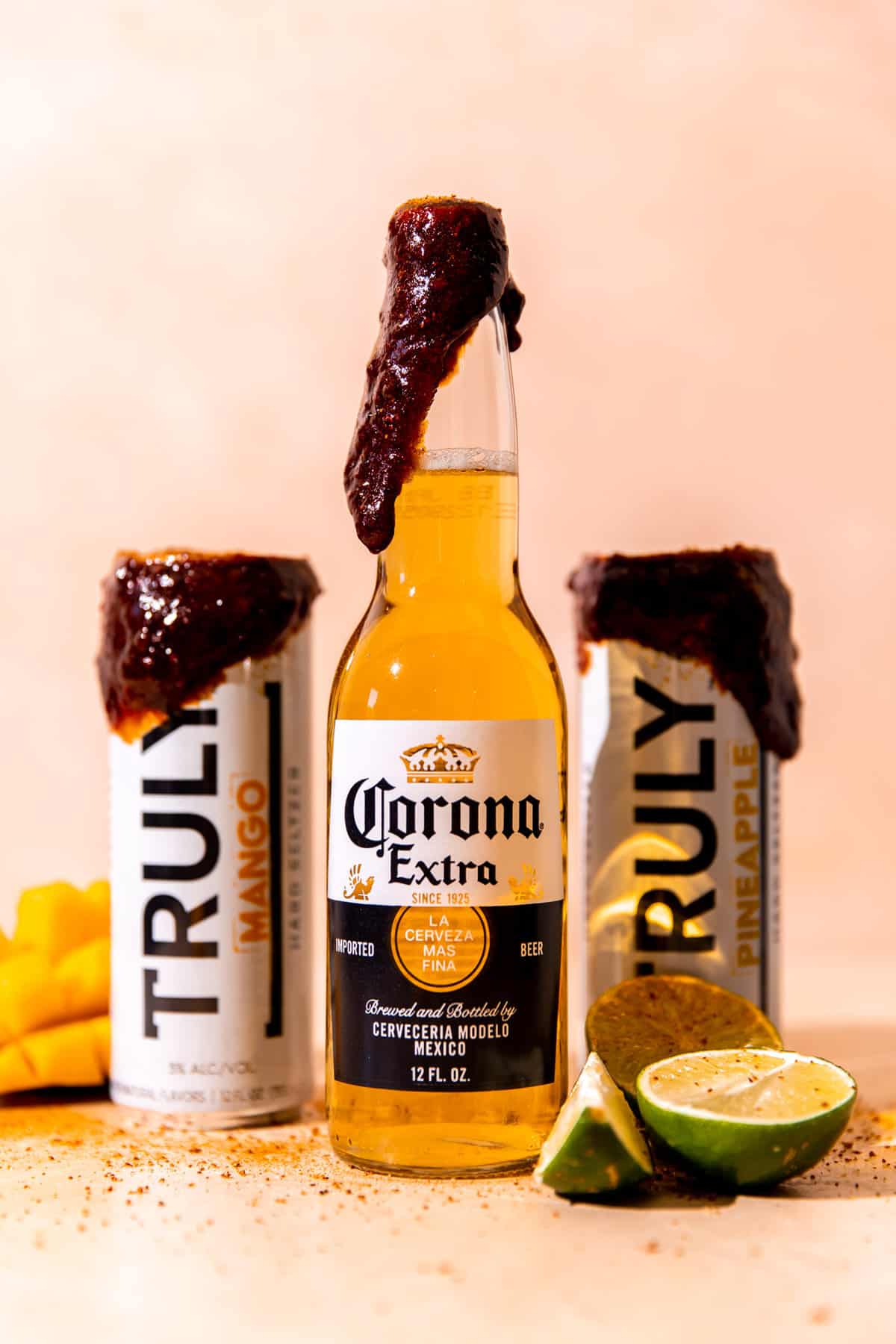 Corona bottle and two hard seltzers with a dark colored chamoy paste on the tops sprinkled with tajin. 