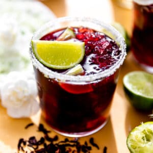 Hibiscus margarita in a glass rimmed with sugar and garnished with a lime wedge.