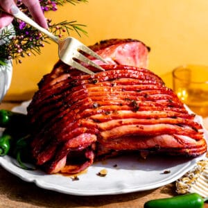 Honey glazed ham with bits of jalapeno on a white plate with a fork separating the slices.