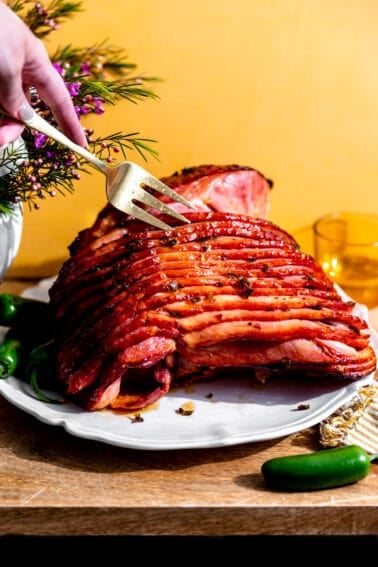 Honey glazed ham with bits of jalapeno on a white plate with a fork separating the slices.
