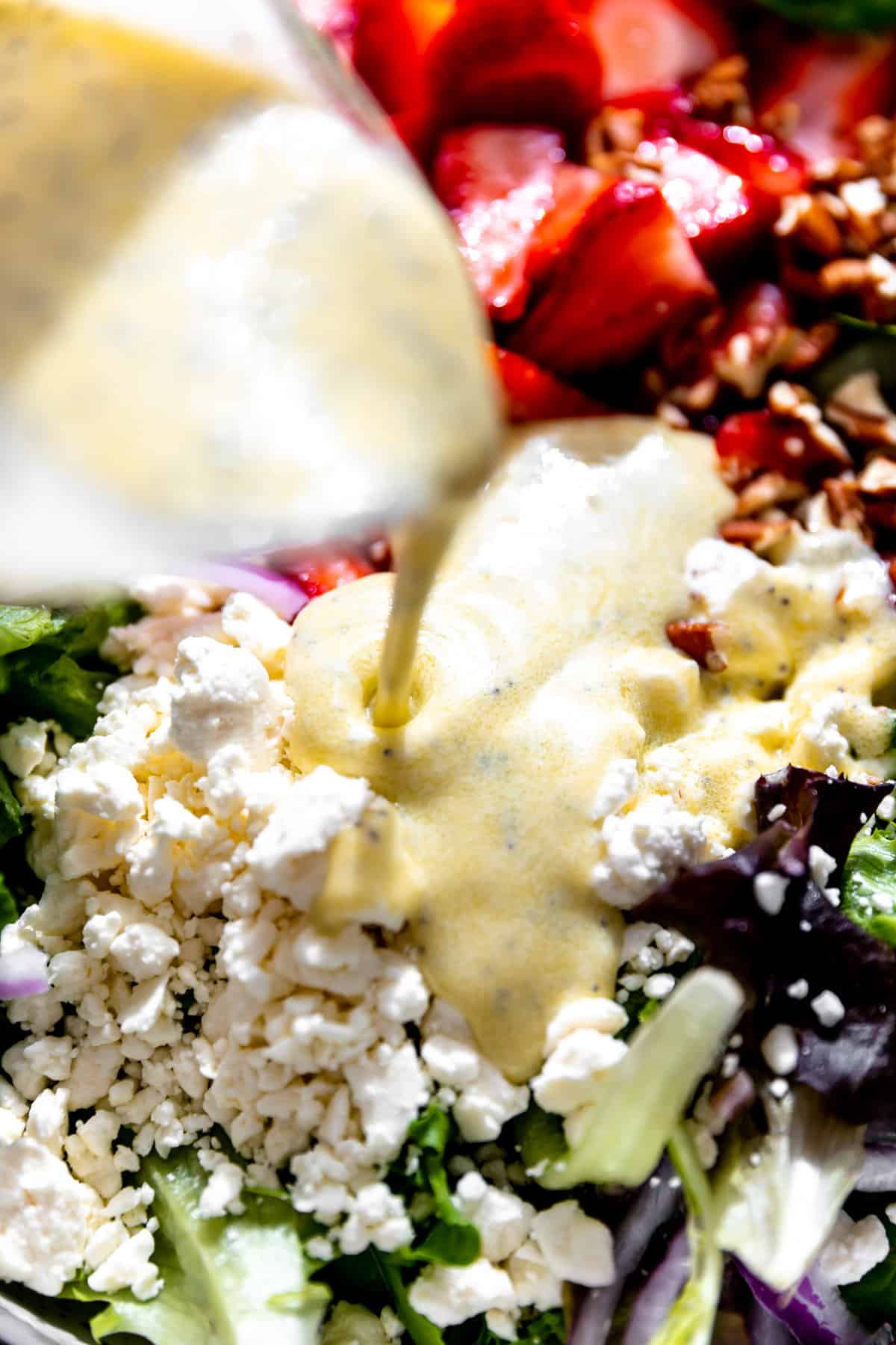 Poppyseed dressing being poured out over a strawberry salad.