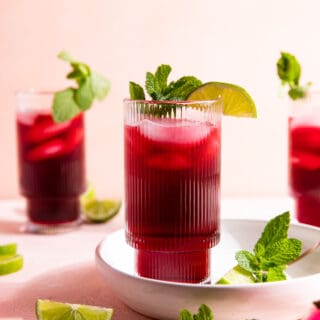 Glasses filled with a dark pink agua de Jamaica topped with lime slices and fresh mint leaves.