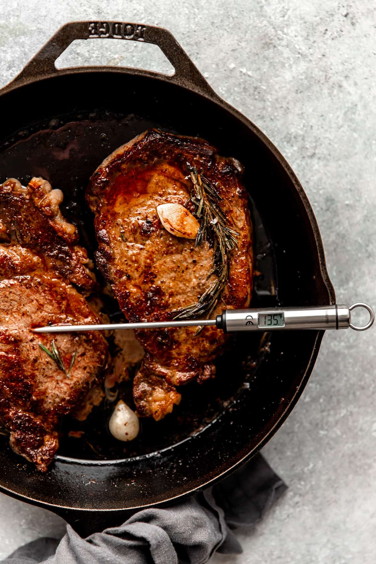 Ribeyes in a cast iron skillet with a thermometer probe showing 135 degrees F.