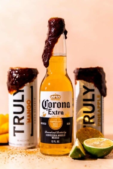 Corona bottle and two hard seltzers with a dark colored chamoy paste on the tops sprinkled with tajin.