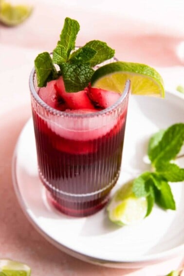 Cup filled with agua de Jamaica on a white plate, garnished with lime and fresh mint.