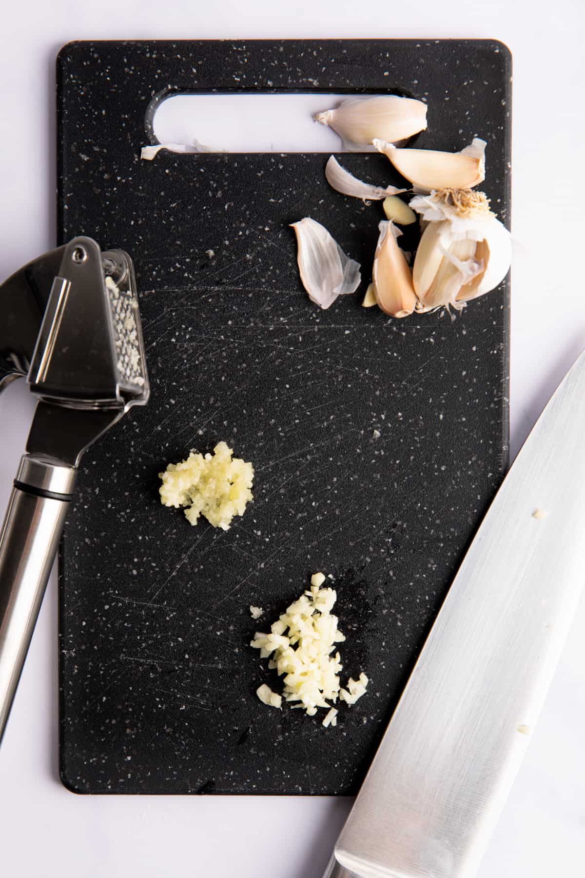 Garlic minced with a knife and with a garlic press on a black cutting board. 