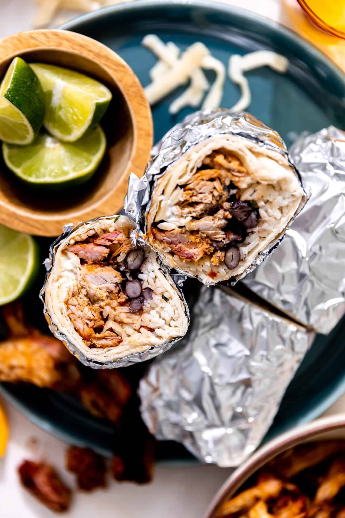 Plate with rolled carnitas burritos wrapped in foil and sliced in half, two ends placed up to show the fillings.