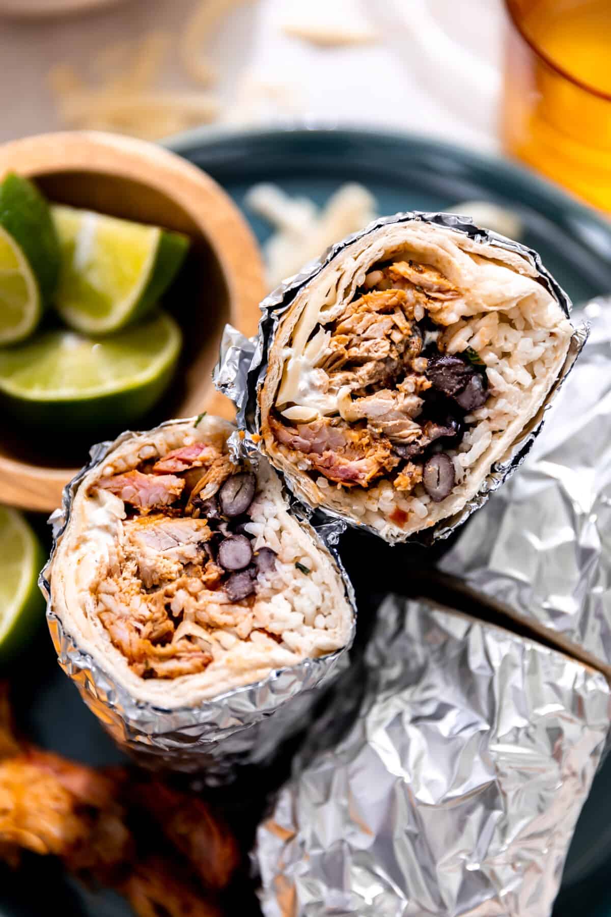Burritos with carnitas, white rice and beans wrapped in foil and sliced in half.