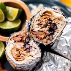 Burritos with carnitas, white rice and beans wrapped in foil and sliced in half.