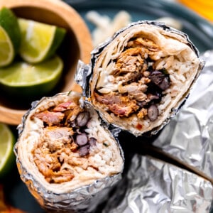 Burritos with carnitas, white rice and beans wrapped in foil and sliced in half.