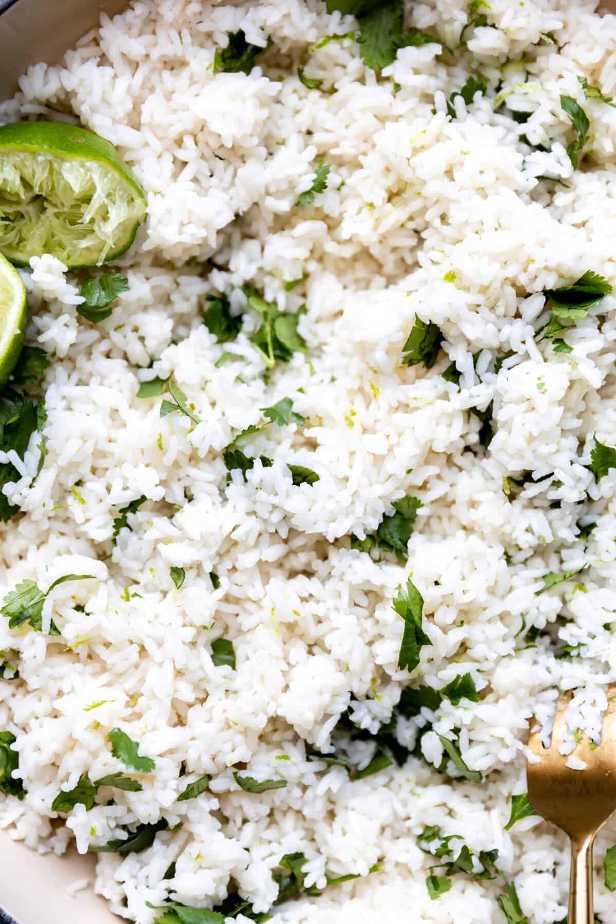 Up close look at cilantro lime rice with specks of fresh cilantro and lime halves that have been juiced.