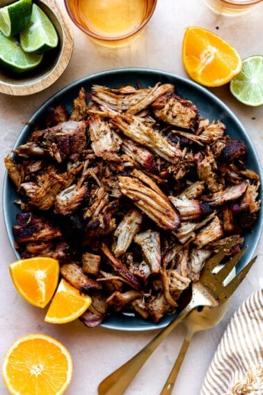 Bowl filled with crispy smoked carnitas meat with orange wedges and lime wedges on the side.