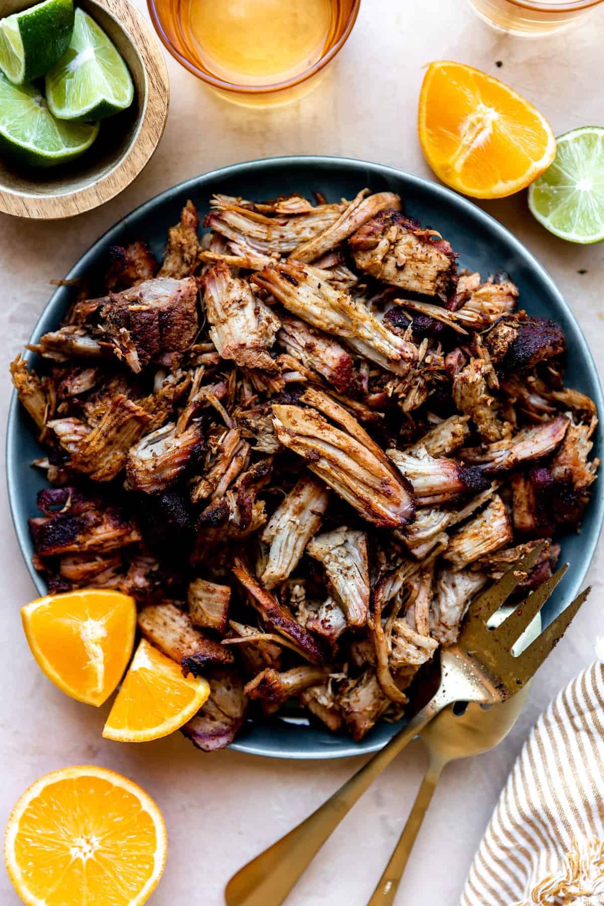 Bowl filled with crispy smoked carnitas meat with orange wedges and lime wedges on the side.